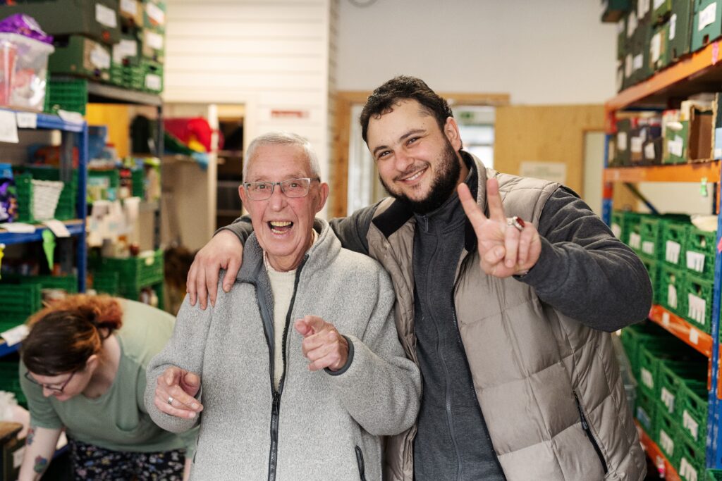 Two smiling male volunteers in the Lisburn Foodbank Warehouse