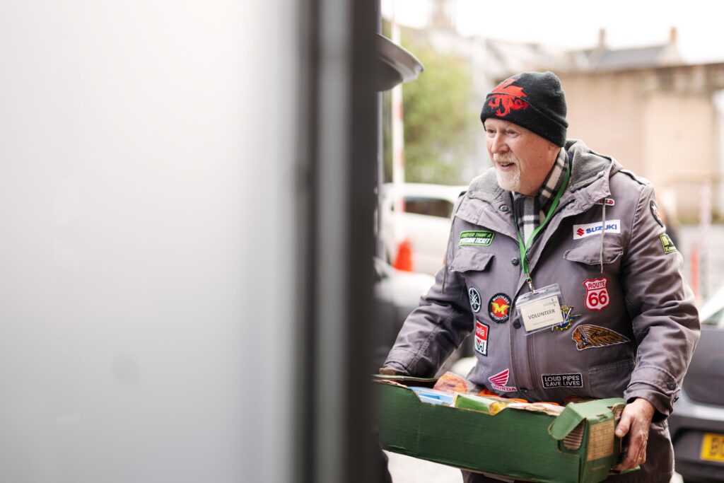 Volunteer with beenie hat, coat and lanyard bringing in donations at the back of the foodbank.